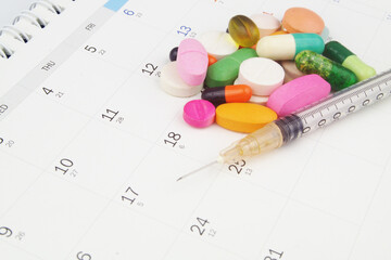 Many drugs and pills with syringe on calendar page