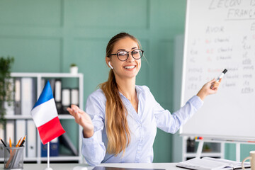 Online foreign languages tutoring. Happy teacher giving French class, pointing at blackboard with...