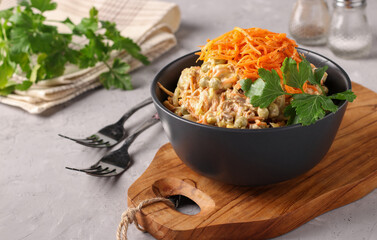 Salad with Korean carrots, meat and canned peas in dark bowl on wooden board