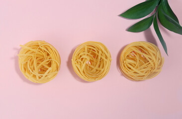 Italian pasta. Spaghetti Capellini isolated on a pink background with a plant, with hard shadows. Pasta in the form of nests. Creative photo of pasta. top view