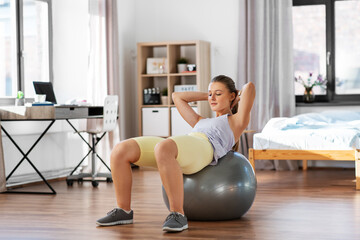 Obraz premium sport, fitness and healthy lifestyle concept - smiling teenage girl exercising with exercise ball at home