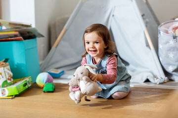 childhood, leisure and people concept - happy little baby girl playing with soft toys at home
