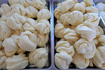 Piles of flower rolls are stacked on metal trays in a restaurant