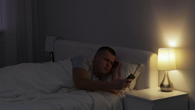 young man waking up to turn off alarm clock on his smartphone and going back to sleep 