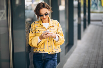 Young woman in yellow jacket using phone outside in the street