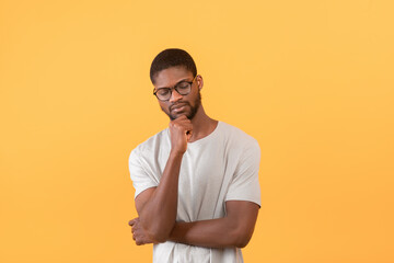 Thoughtful african american guy touching chin and thinking about something, standing over yellow background