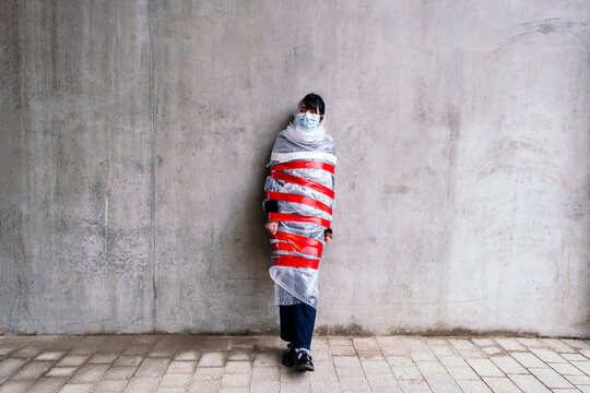 Woman wearing protective face mask wrapped in bubble wrap on footpath