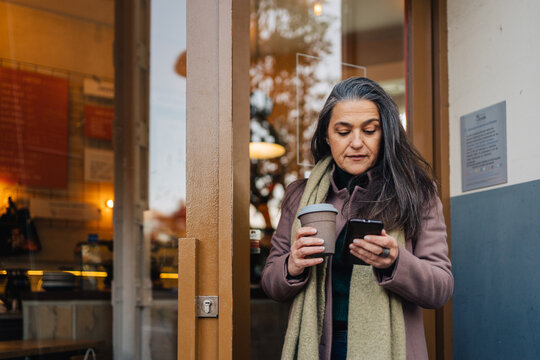 Ethnic woman with cup of coffee browsing smartphone
