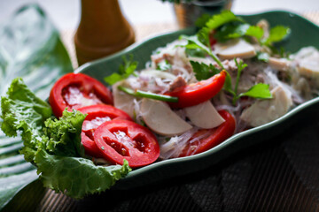 Spicy vietnamese sausages salad placed in a leaf-shaped green plate. With onion, garlic, red pepper on a black wooden table