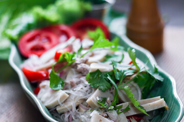 Spicy vietnamese sausages salad placed in a leaf-shaped green plate. With onion, garlic, red pepper on a black wooden table