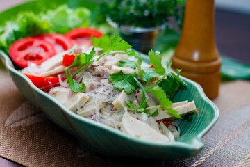 Spicy vietnamese sausages salad placed in a leaf-shaped green plate. With onion, garlic, red pepper on a black wooden table