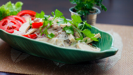 Spicy vietnamese sausages salad placed in a leaf-shaped green plate. With onion, garlic, red pepper on a black wooden table