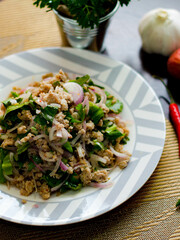 Ground pork salad placed in white and gray plates with onions, garlic, red chillies on a black wooden table.