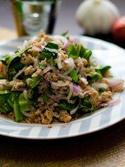 Ground pork salad placed in white and gray plates with onions, garlic, red chillies on a black wooden table.