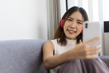 Lifestyle home life Asian woman sits using her mobile phone and listens to music on the sofa in the living room.