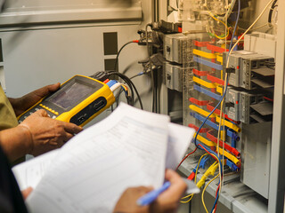 Electrician engineer uses a multimeter to test the electrical installation and power line current in an electrical system control cabinet.