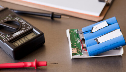 red polymeter work table. in the background multimeter and powerbank with blu batteries mod 18650