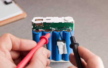 Charge indicator circuit, multimeter red and black poles in the hands of man checking voltage and...