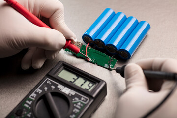 Charge indicator circuit, multimeter red and black poles in the hands of man checking voltage and...