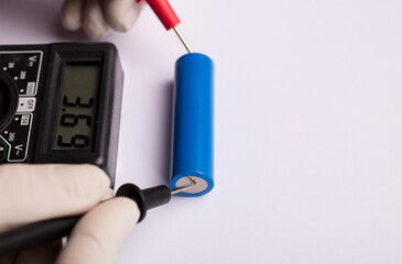18650 blue battery, multimeter red and black poles in the hands of man checking voltage and amps with white background,