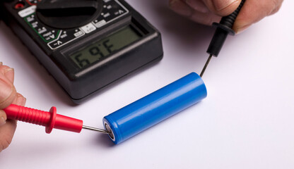 18650 blue battery, multimeter red and black poles in the hands of man checking voltage and amps...