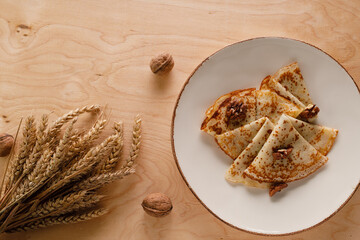 Homemade pancakes with walnuts on a wooden table. Pancake day. Decorated with ears of wheat.