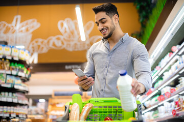 Middle Eastern Male Customer Texting On Phone Shopping Groceries In Supermarket