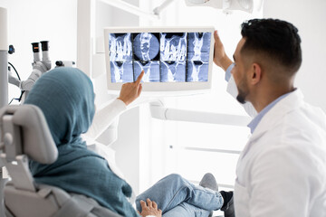 Obraz premium Male Dentist Showing Teeth Xray Picture On Digital Monitor To Muslim Woman