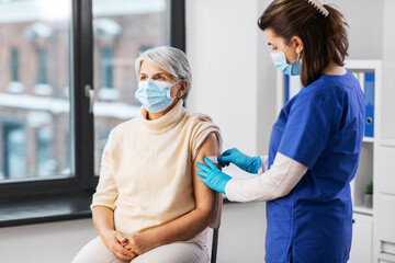 Obraz premium medicine, health and vaccination concept - doctor or nurse applying medical patch to vaccinated senior woman in mask at hospital