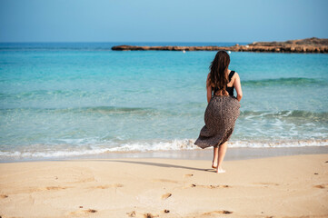 Back view of woman walking with bare feet on sandy beach