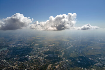 Aerial view from airplane window at high altitude of distant city covered with puffy cumulus clouds...