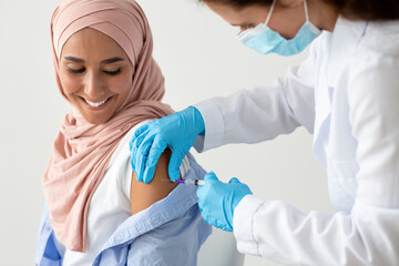 Closeup Shot Of Female Doctor Making Coronavirus Vaccine Injection To Muslim Woman - obrazy, fototapety, plakaty