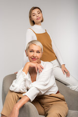 Fototapeta premium joyful young woman near smiling mother sitting in armchair isolated on grey