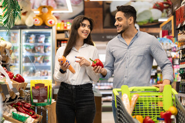 Happy Middle Eastern Spouses Choosing Vegetables During Grocery Shopping In Supermarket