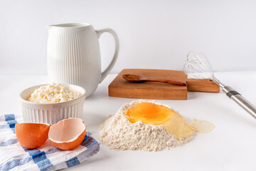Baking ingredients flour, sugar, egg, beater, on a white background, copy space. Egg with yolk in flour on the table.