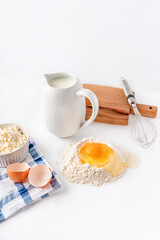 Baking ingredients flour, sugar, egg, beater, on a white background, copy space. Egg with yolk in flour on the table.