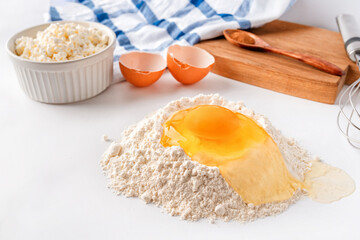 Baking ingredients flour, sugar, egg, beater, on a white background, copy space. Egg with yolk in flour on the table.