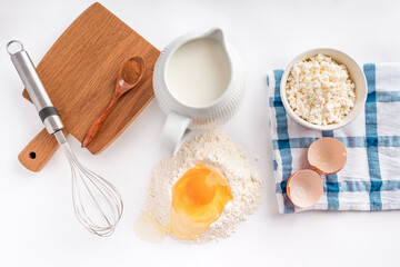 Baking ingredients flour, sugar, egg, beater, on a white background, copy space. Egg with yolk in flour on the table.