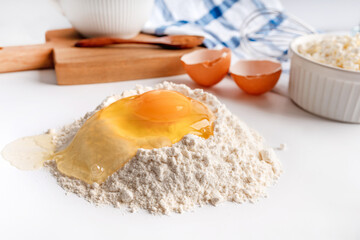 Baking ingredients flour, sugar, egg, beater, on a white background, copy space. Egg with yolk in flour on the table.