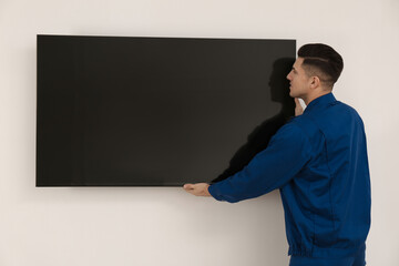 Professional technician installing modern flat screen TV on wall indoors - obrazy, fototapety, plakaty