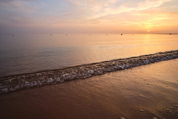 Calm sea shore with crushing waves on sandy beach at sunrise