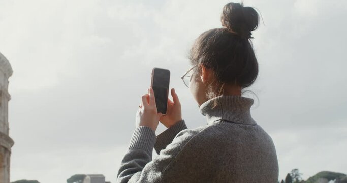 A young woman photographs the Colosseum on a mobile phone