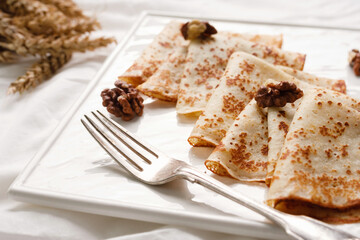 Homemade pancakes with walnuts and honey on a white fabric background. Pancake day.