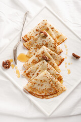 Homemade pancakes with walnuts and honey on a white fabric background. Pancake day.