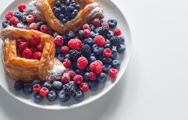 Danish with raspberries and blueberries on  round plate with berries on  white table