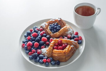 Danish with raspberries and blueberries with cup of tea on  white table