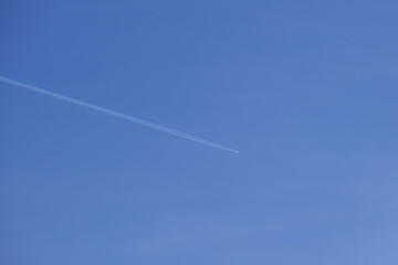 Distant passenger jet plane flying on high altitude on clear blue sky leaving white smoke trace of contrail behind. Air transportation concept