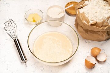 the process of making dough for pancakes with ingredients on a light table, eggs and flour are whipped with a mixer