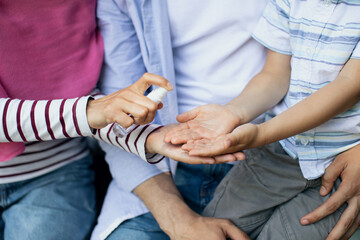 Closeup Shot Of Family With Little Son Applying Disinfectant Spray On Hands