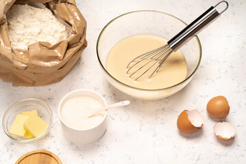 the process of making dough for pancakes with ingredients on a light table, eggs and flour are whipped with a mixer